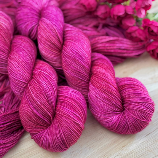 Three skeins of pink yarn on a wooden surface with pink flowers in the background