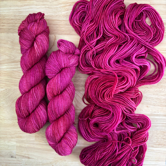 Skeins of hand dyed pink yarn on a light wooden surface