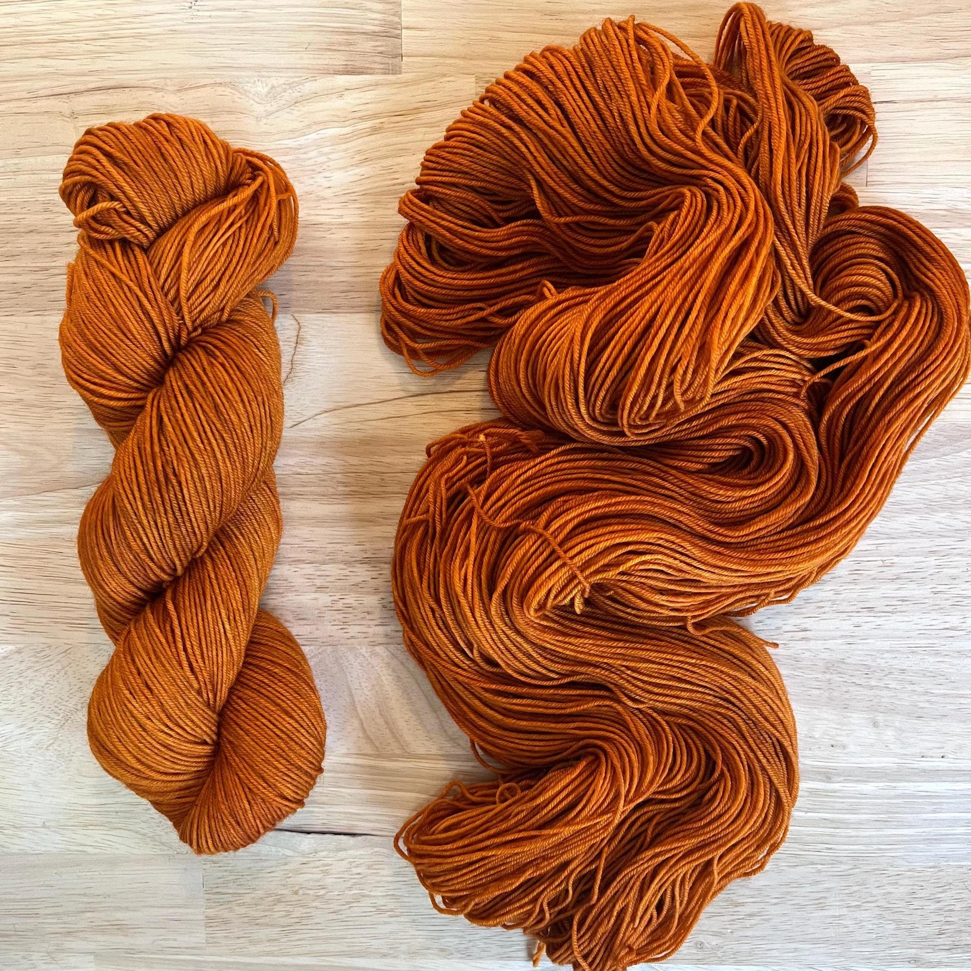 Warm rust copper orange hand dyed merino wool yarn arranged in a skein on a wood background.