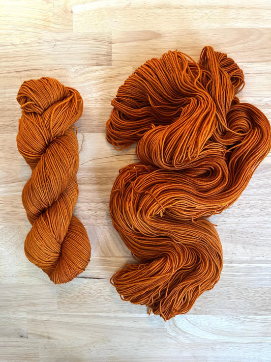 Warm rust copper orange hand dyed merino wool yarn arranged in a skein on a wood background.