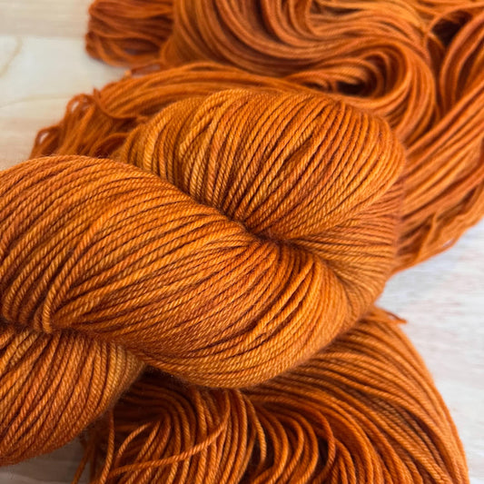Warm rust copper orange hand dyed merino wool yarn arranged in a skein on a wood background.