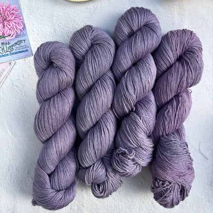 Three skeins of purple yarn on a light surface with a teacup and lemon.