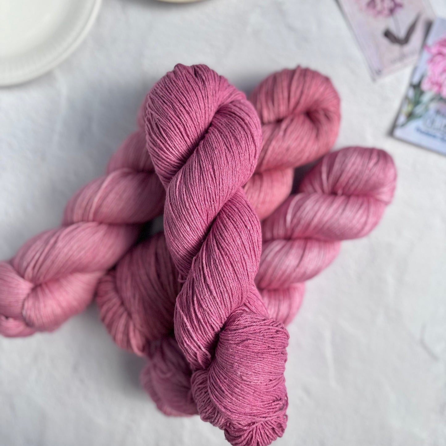 Skeins of pink yarn on a white surface with a cup of tea and saucer in the background.