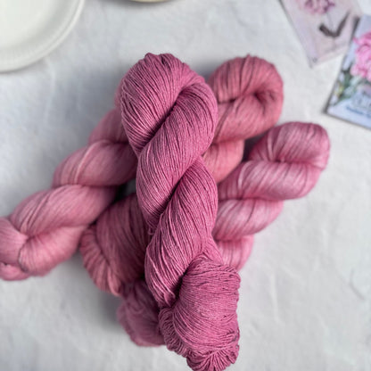 Skeins of pink yarn on a white surface with a cup of tea and saucer in the background.