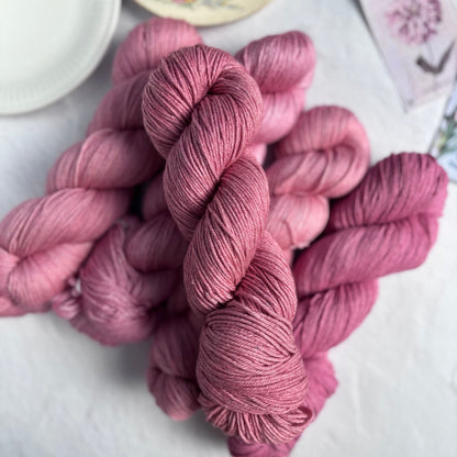Pink yarn skeins on a white surface with a cup of tea in the background