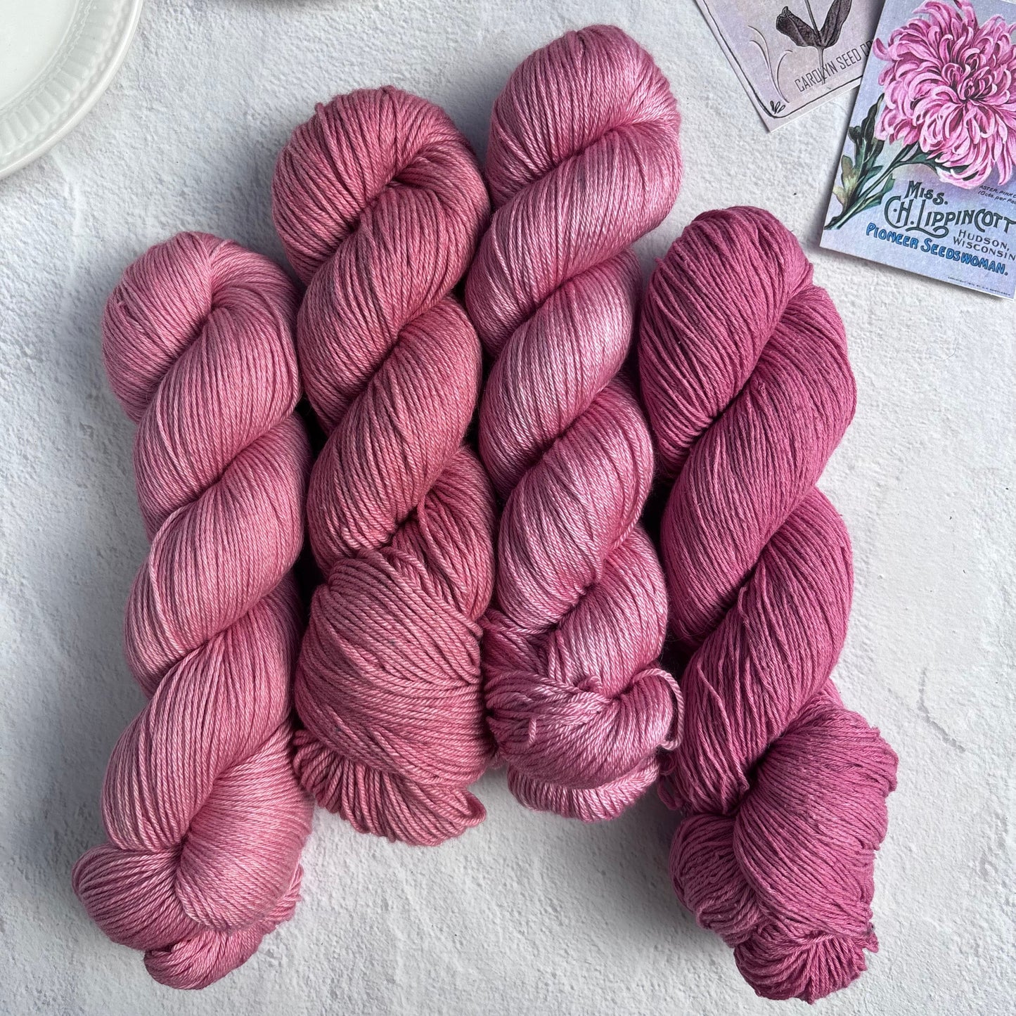 Pink yarn skeins on a light surface with a cup of tea and seed packets.