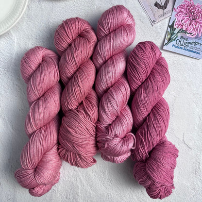 Pink yarn skeins on a light surface with a cup of tea and seed packets.