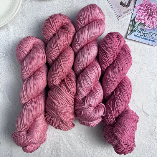 Pink yarn skeins on a light surface with a cup of tea and seed packets.