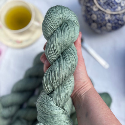 Hand holding a skein of green yarn with a blurred background