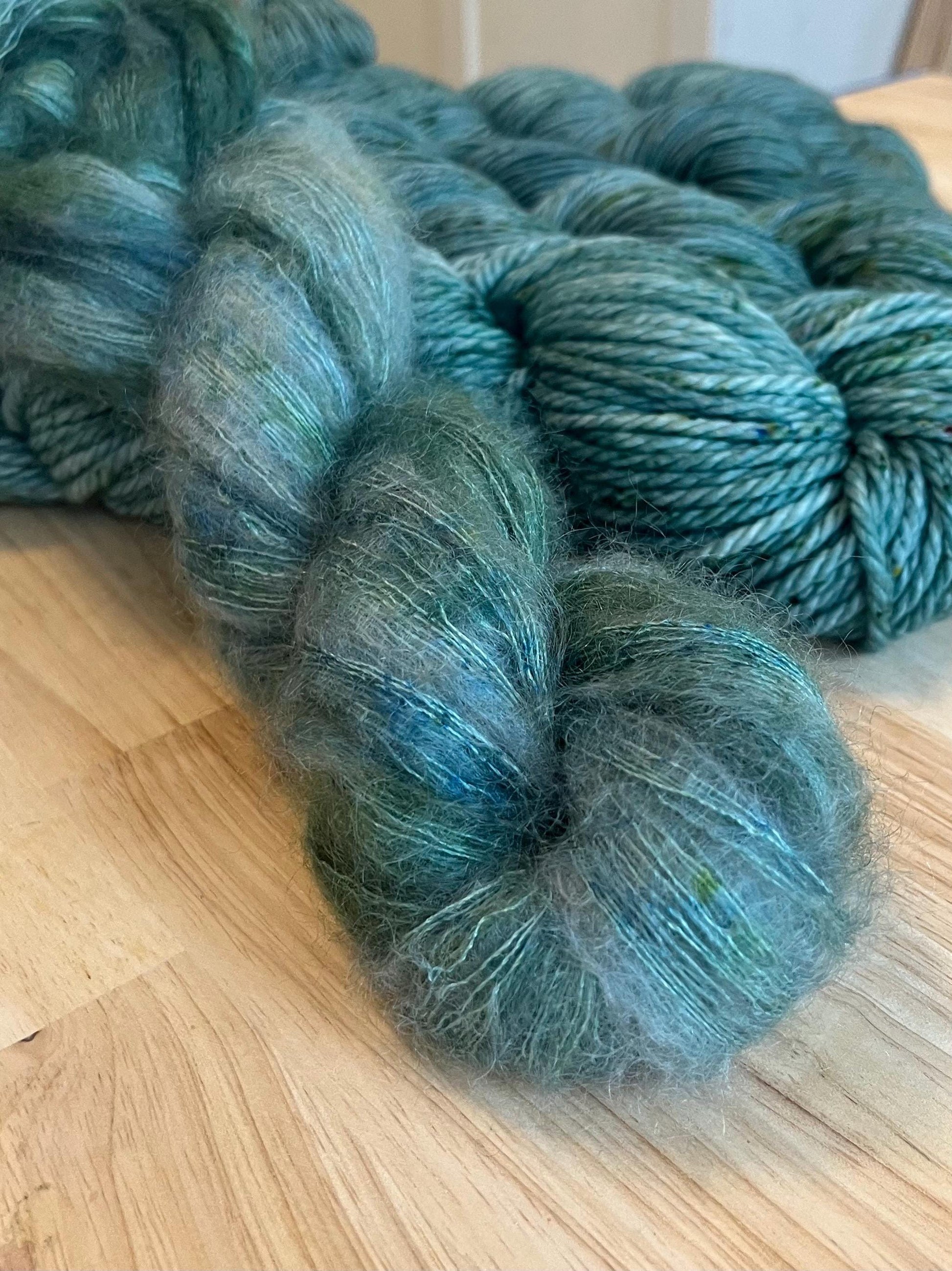 A skein of hand dyed silvery sage green mohair silk lace yarn with green speckles.