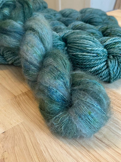 A skein of hand dyed silvery sage green mohair silk lace yarn with green speckles.