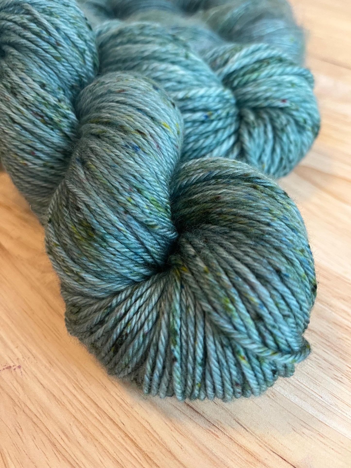 A skein of Worsted weight  hand dyed silvery sage green merino wool yarn with green speckles.