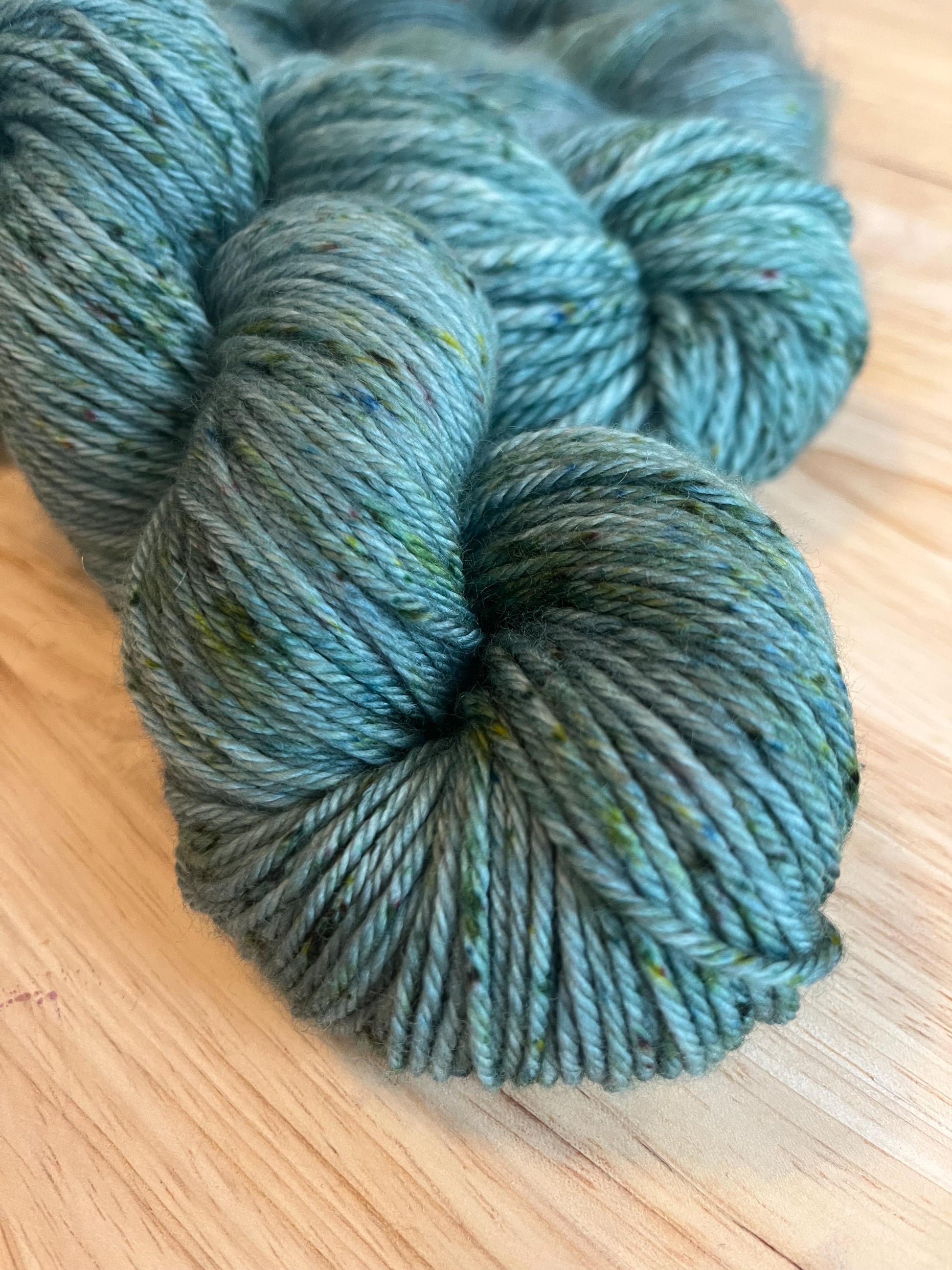 A skein of Worsted weight  hand dyed silvery sage green merino wool yarn with green speckles.