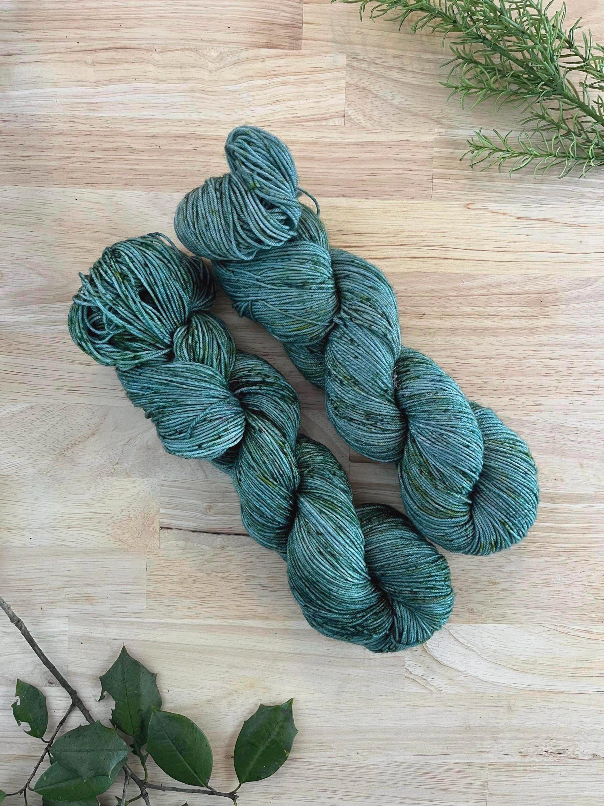 Two skeins of hand dyed gray green yarn with green speckles.