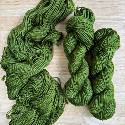 Three skeins of green hand dyed yarn on a light wooden surface