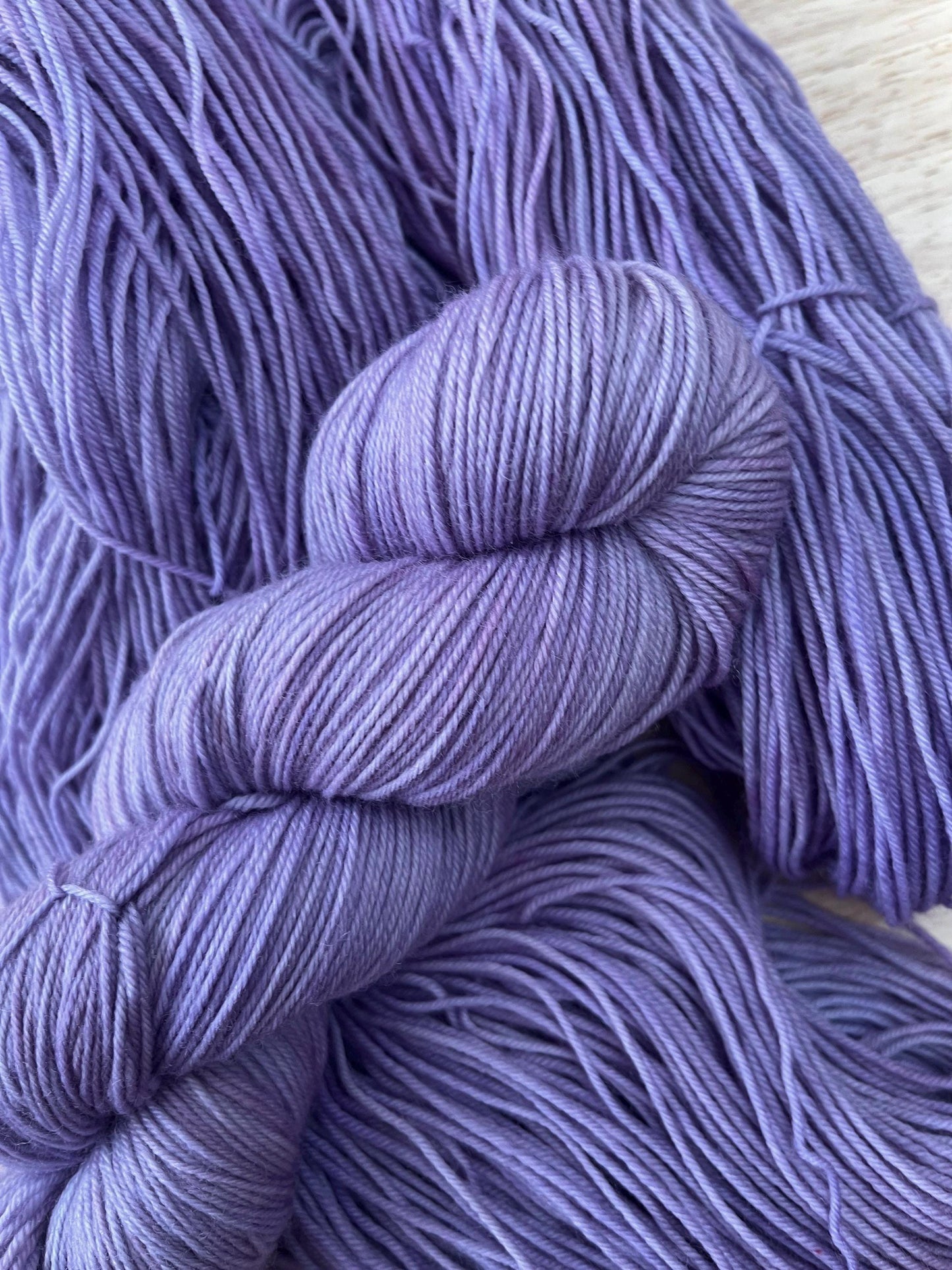 A skein of hand dyed light purple merino yarn against a wooden background.
