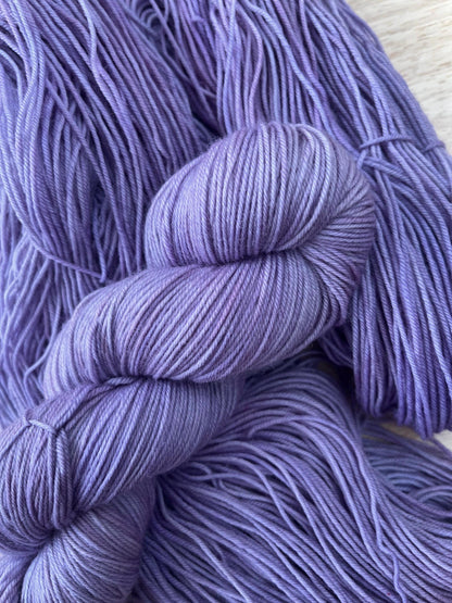 A skein of hand dyed light purple merino yarn against a wooden background.