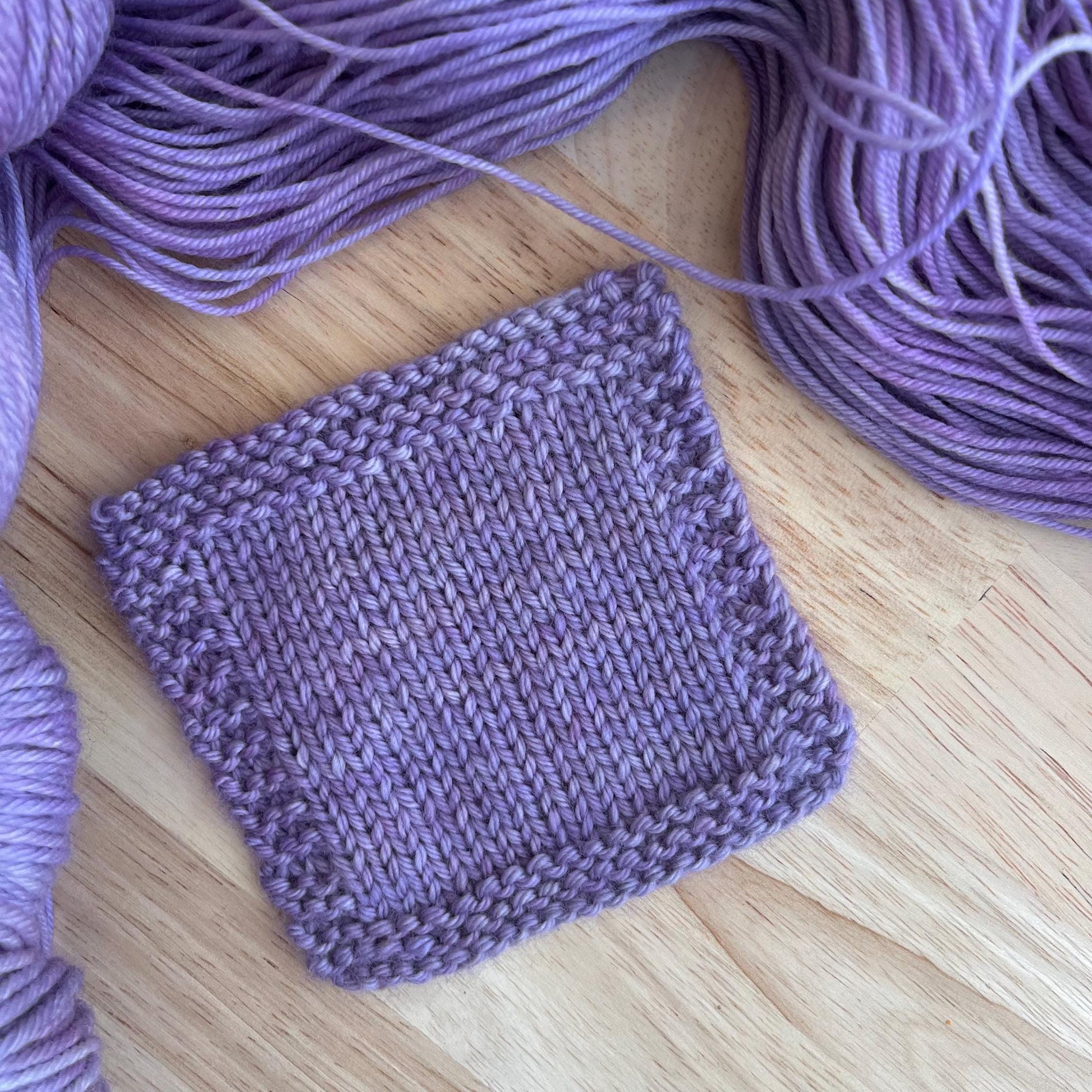 A knit swatch of hand dyed purple gray yarn.