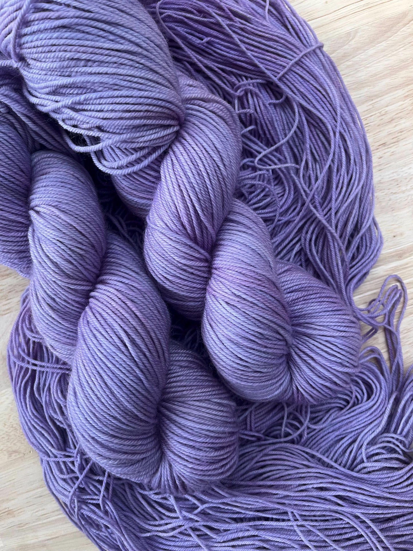 Skeins of hand dyed light purple wool yarn against a wooden background.