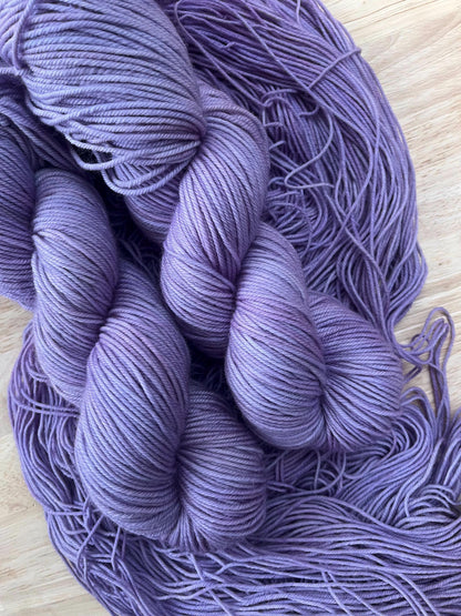 Skeins of hand dyed light purple wool yarn against a wooden background.