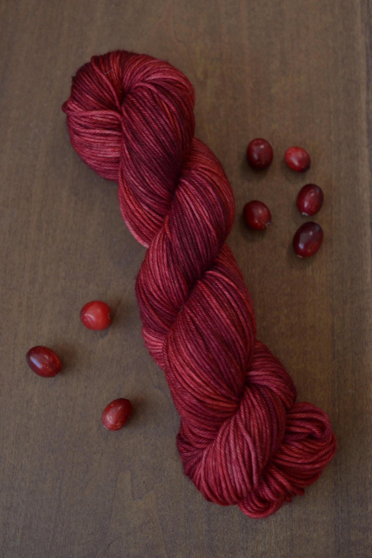Hank of dark red wool yarn on a dark wood background surrounded by cranberries.