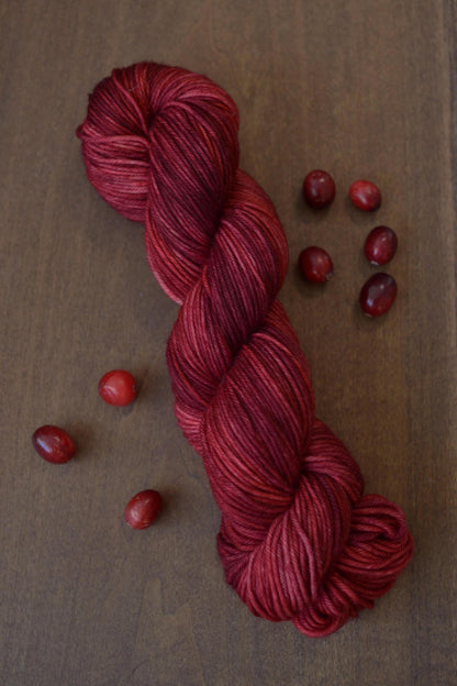 Hank of dark red wool yarn on a dark wood background surrounded by cranberries.